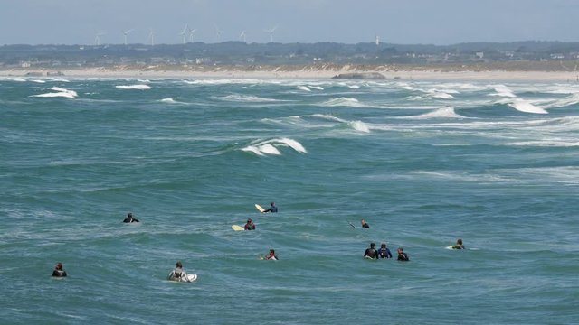 Tens of water surfers lie on their boards in the sea, waiting for a good wave.