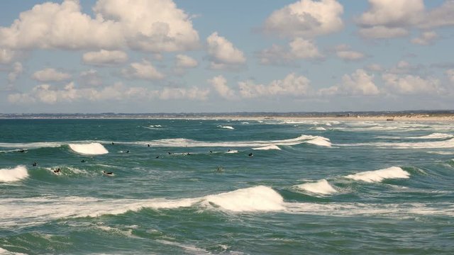 Surfers lie in the water like penguins, waiting for the perfect wave. A few of them attempt the smaller waves.