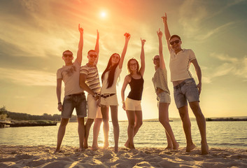 Obraz premium Friends funny dance on the beach under sunset sunlight.
