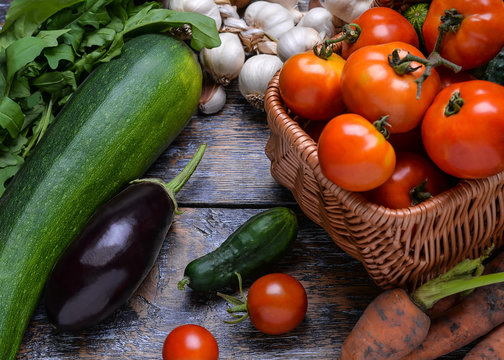 Harvest Vegetables: tomatoes, cucumbers, zucchini, eggplant, onion, garlic, arugula on the wooden background