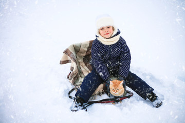 Little girl and a red cat on the sleigh.