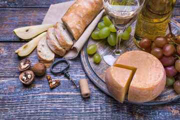 White wine in a bottle, cork bottle screw and a set of products - cheese, grapes, nuts, olives, figs on a wooden background