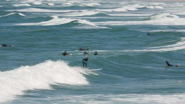 A young, inexperienced surfer manages to ride a wave, surrounded by surfers wading in the ocean, waiting for that big wave.