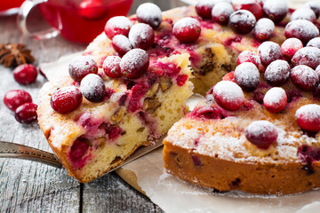 Slice of homemade cranberry cake with walnuts, berries and powdered sugar on the old wooden fone. Space for text. Rustic style. Selective focus.