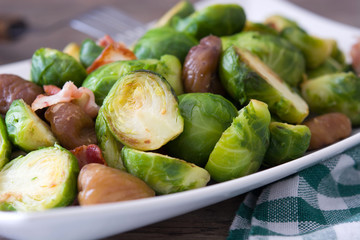 Brussels sprouts with chestnuts and bacon on wooden table
