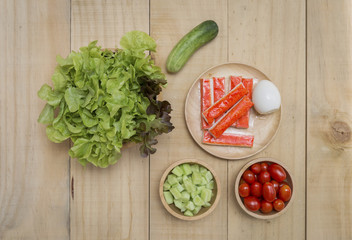 Green lettuce and cucumber with tomato salad with crab stick on wood background