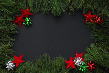 Fototapeta na wymiar Frame of pine branches decorated with red stars of felt and bows of red, green and silver color. Christmas/New Year decorations Black background, top view, flat lay, copy space