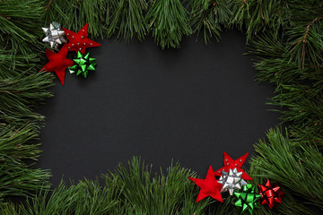 Frame of pine branches decorated with red stars of felt and bows of red, green and silver color. Christmas/New Year decorations  Black background, top view, flat lay, copy space