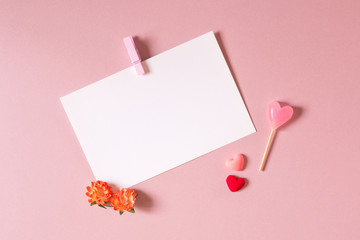 Valentine day composition: stationery / photo template with clamp, small hearts, candy and spring flowers on light pink background. Top view.