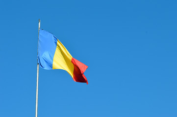 Romanian flag blowing in wind on flagpole isolated against blue sky
