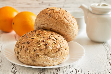 Whole wheat buns with mixed seeds with teapot and oranges in background on white rustic table. Concept image for healthy breakfast