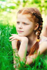 Fototapeta premium Beautiful redhead Girl in the green grass in Summer - Portrait of Child with Red Hair