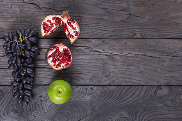 grapes and sliced fruit, pomegranates, apples on a black wooden table