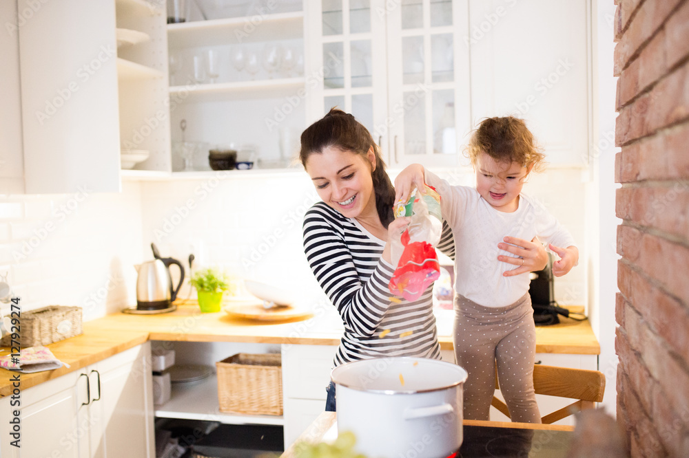 Wall mural Mother with her daughter in the kitchen cooking together