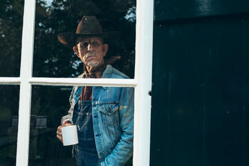 Farmer with beard and hat holding cup of coffee looking out wind