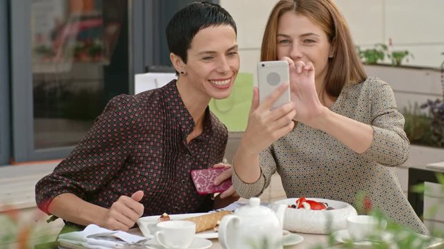 Smiling beautiful women talking selfie with smart phone while having lunch in the street cafe