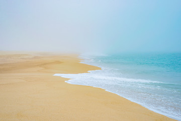 Sandy beach coast in fog, sea wave foam ocean romantic mist