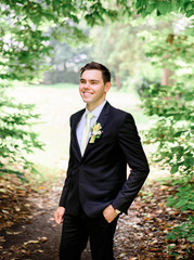young handsome groom in a black suit standing alone outdoors