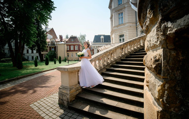 young and beautiful bride in white dress standing on the stairs