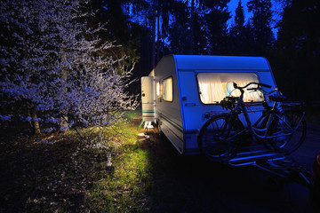 Caravan trailer on a forest road under a blooming tree in Spring