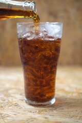 A glass of cola being poured into ice glass