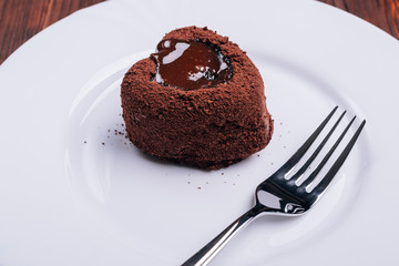 Fork and chocolate cake in the shape of a heart on a white plate