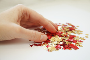a hand picking, holding, taking red and gold sequins on a white