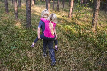 Young child boy (brother) giving his sister piggyback outdoors in the forest. Children summer activities.