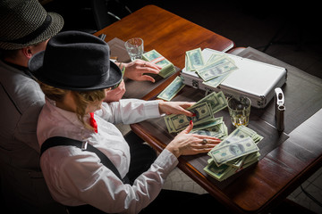 Elegant girl and man on gangster party. Mafia party in restaurant. man and woman share the money won. Man and woman at the table divided money. Woman and man counts the money
