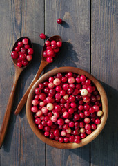 Fresh red forest cranberry in a round bowl with a wooden spoons on a wooden table surface. Autumn harvest of wild berries