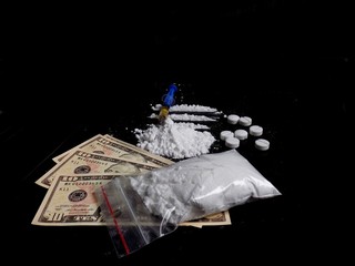 Injection syringe on cocaine drug powder lines and pile, pills and cocaine bag on dollar bills money on black background