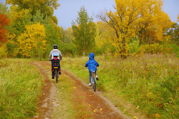 Family on bikes in golden autumn park, father and kids cycling on trail, active sport with children outdoors
