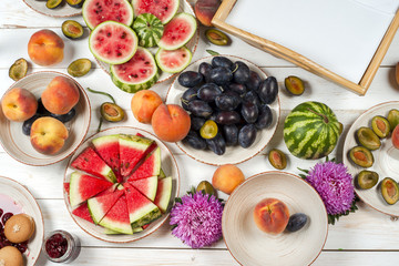 Colorful fruit set of purple, red and orange background in bowls. Plum, peaches, watermelon sliced above white tabletop