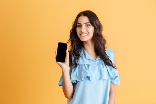 Smiling brunette woman in blue dress showing blank smartphone screen