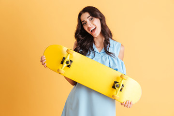 Portrait of a smiling excited brunette woman holing skateboard