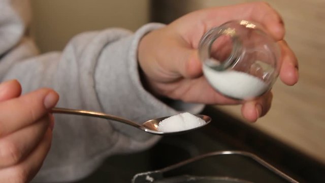 Man pours sugar on a spoon from the jar