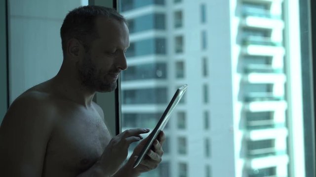 Young man using tablet computer standing by window at home
