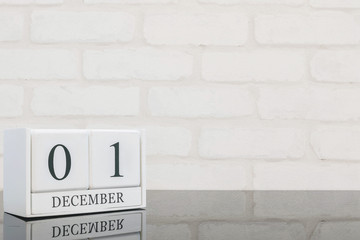Closeup white wooden calendar with black 1 december word on black glass table and white brick wall textured background with copy space , selective focus at the calendar