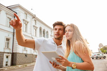 Couple holding tablet while he points finger away at something