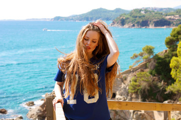 Young woman enjoying her time on the top of the rock, beautiful landscape of mediterranean sea and green natural harbour bay on the background. Pretty girl in t-shirt with great hair and cute smile.