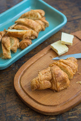 Slices of croissant and cubes of white chocolate on a wooden board with slices on a  turquoise ceramic platter out of focus, in the background