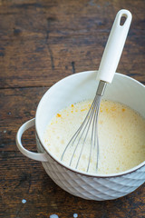 Custard or pudding making with whole milk, eggs and sugar, in a white vintage pot with wooden table background and splashes of milk