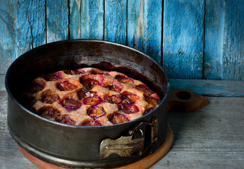 Pie with plums in a metal baking dish, an old blue background, space for text