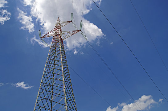 High Voltage Power Lines intersect at a large metal Utility pole in Maine against  blue sky.