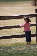 young girl looking through split rail fence into open field with wind blowing hair