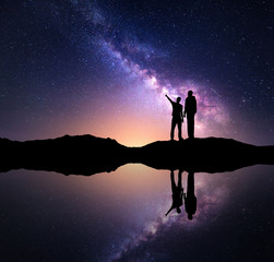 Milky Way with silhouette of a family. Father and a son who pointing finger in night starry sky on...