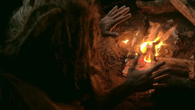 Neanderthal man warms his hands by the first bonfire in his cave