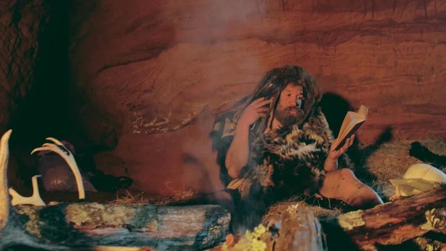 Neanderthal man reads old book near bonfire in his cave