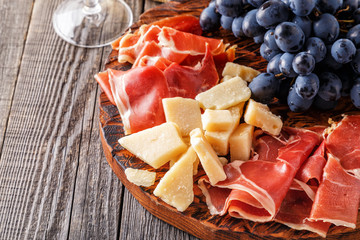Prosciutto, wine, grape, parmesan on wooden table.