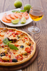 Big tasty pizza with seafood, tomatoes, wine on wooden table